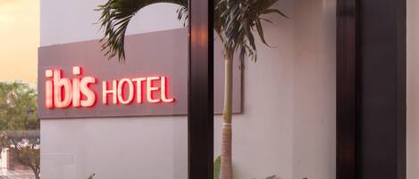Señal de hotel Ibis con área de estar al aire libre y una palmera.