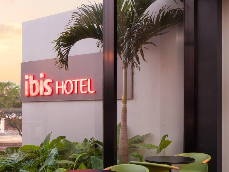 An ibis hotel sign with outdoor seating and a palm tree.