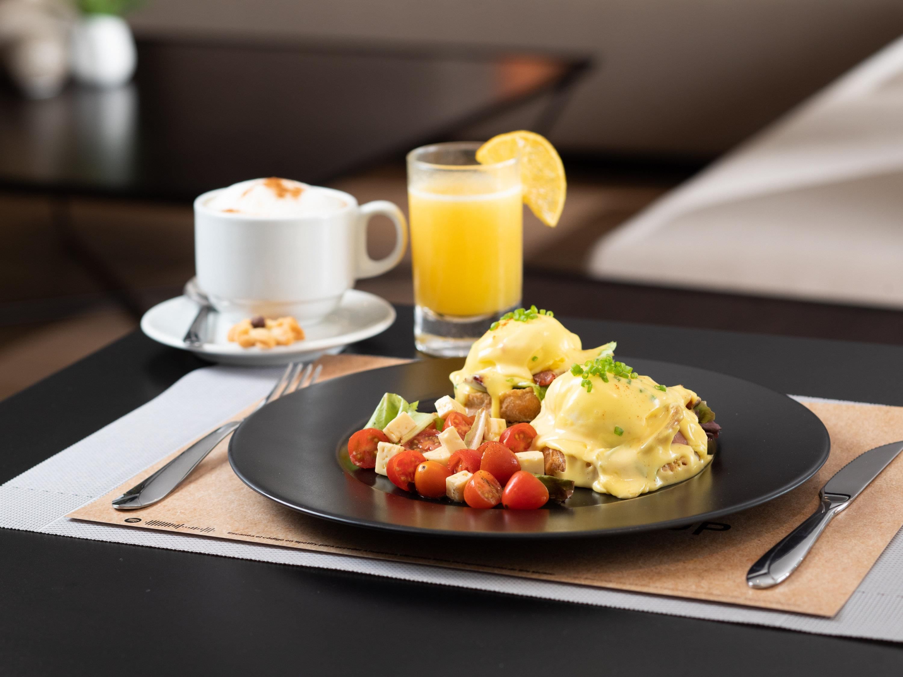 Un desayuno con huevos benedictinos, un vaso de jugo de naranja y una taza de café sobre una mesa.