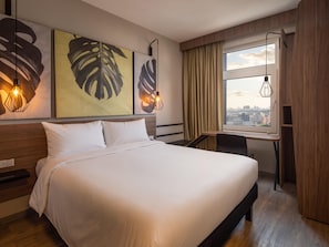 Hotelkamer met een groot bed, een bureau, een stoel, een raam met gordijnen en kunst aan de muur.