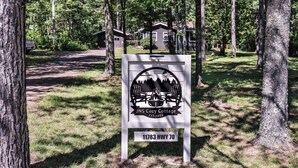 En skylt för JNS Cozy Cottage med en skog i bakgrunden.
