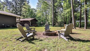 Ett trädäck med Adirondack-stolar, en eldstad och ett litet träbord.