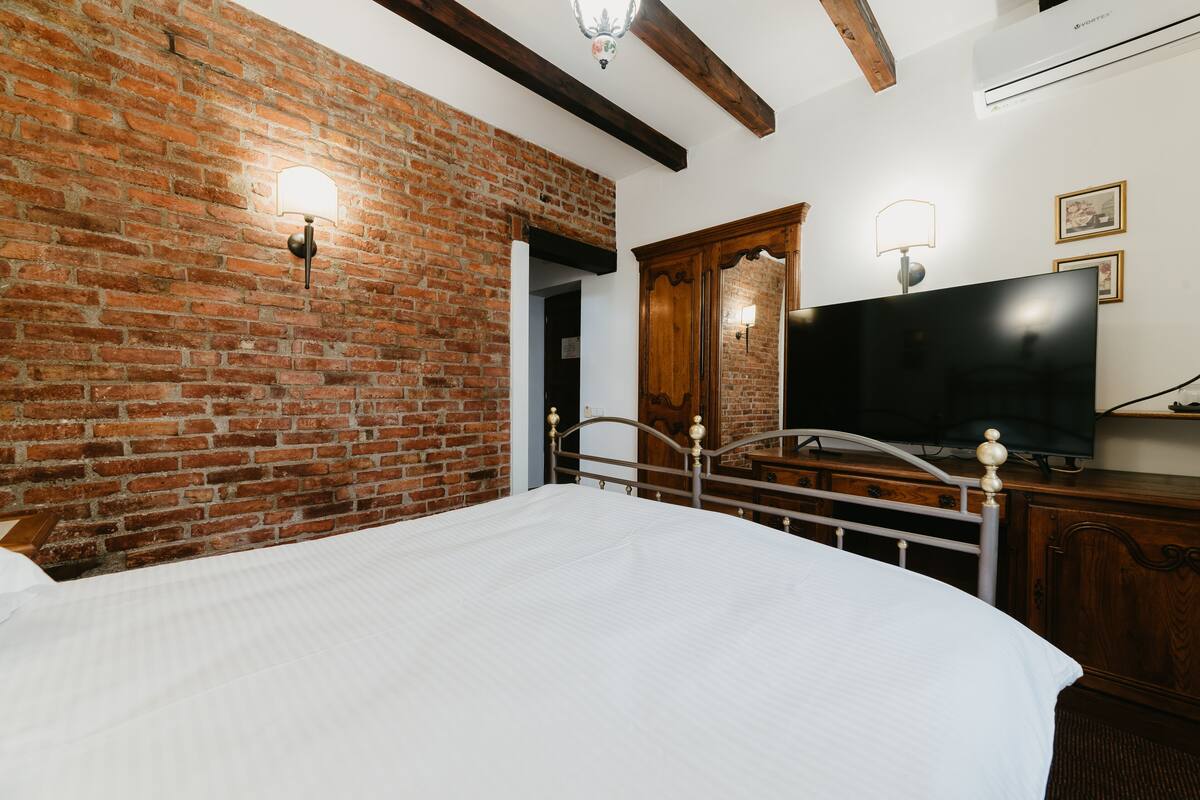 Ein Zimmer mit Backsteinwand, einem Bett mit weißer Bettdecke, einem Holzschrank, einem Fernseher und einer Wandleuchte.