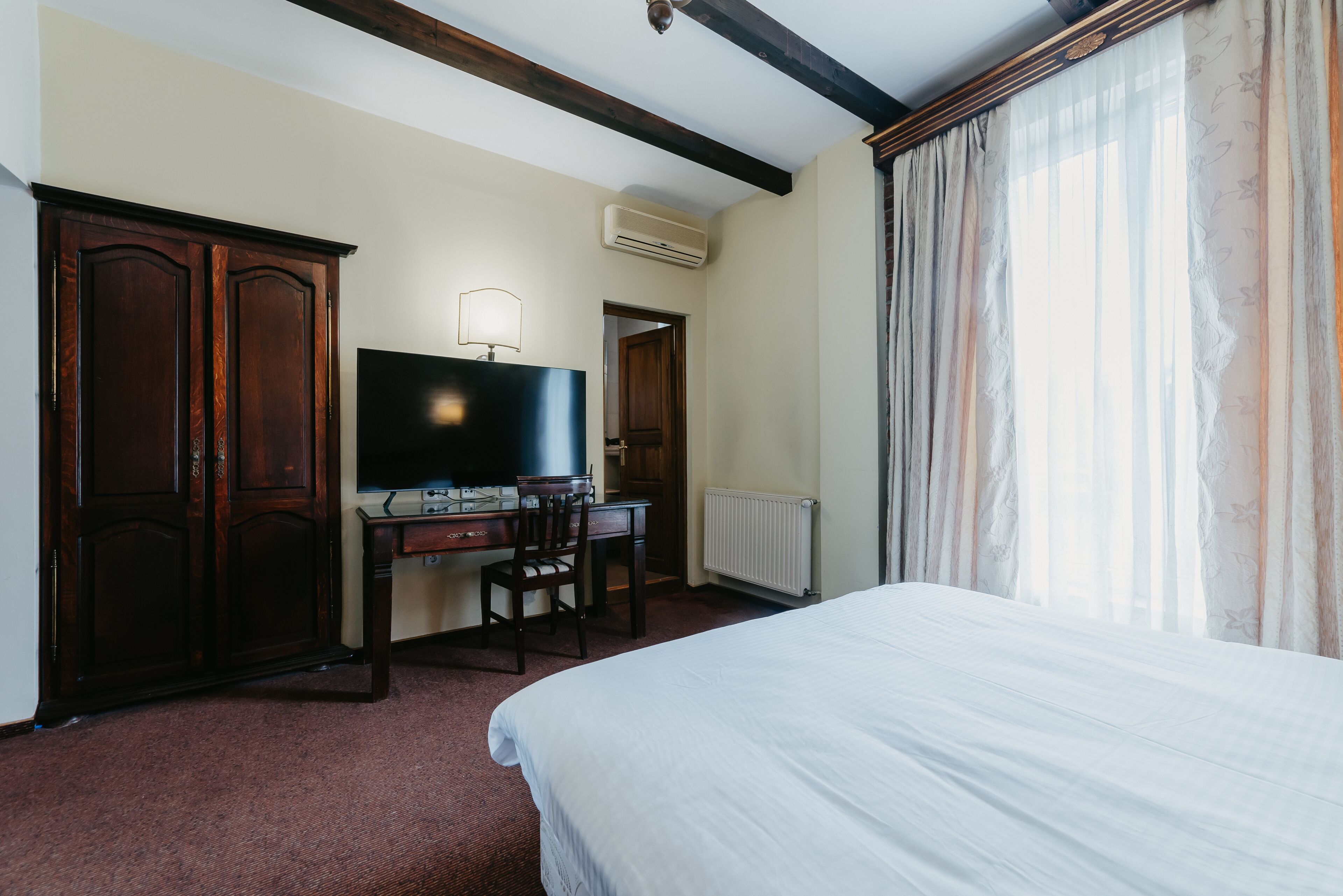 Una habitación de hotel con cama, escritorio, silla, televisor y armario.