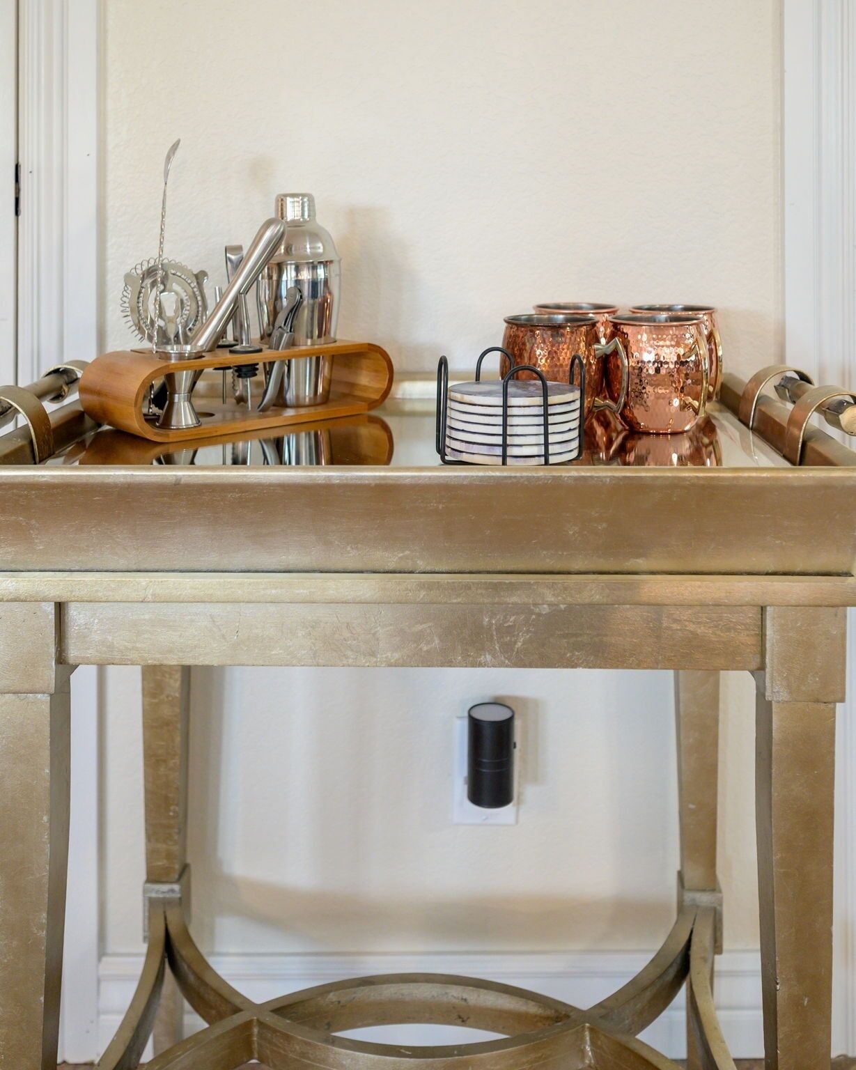 A table with a tray holding kitchen utensils, a stack of plates, and copper mugs.