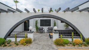 Um pátio moderno ao ar livre com um caminho de pedra, duas cadeiras cinzentas e uma mesa pequena.