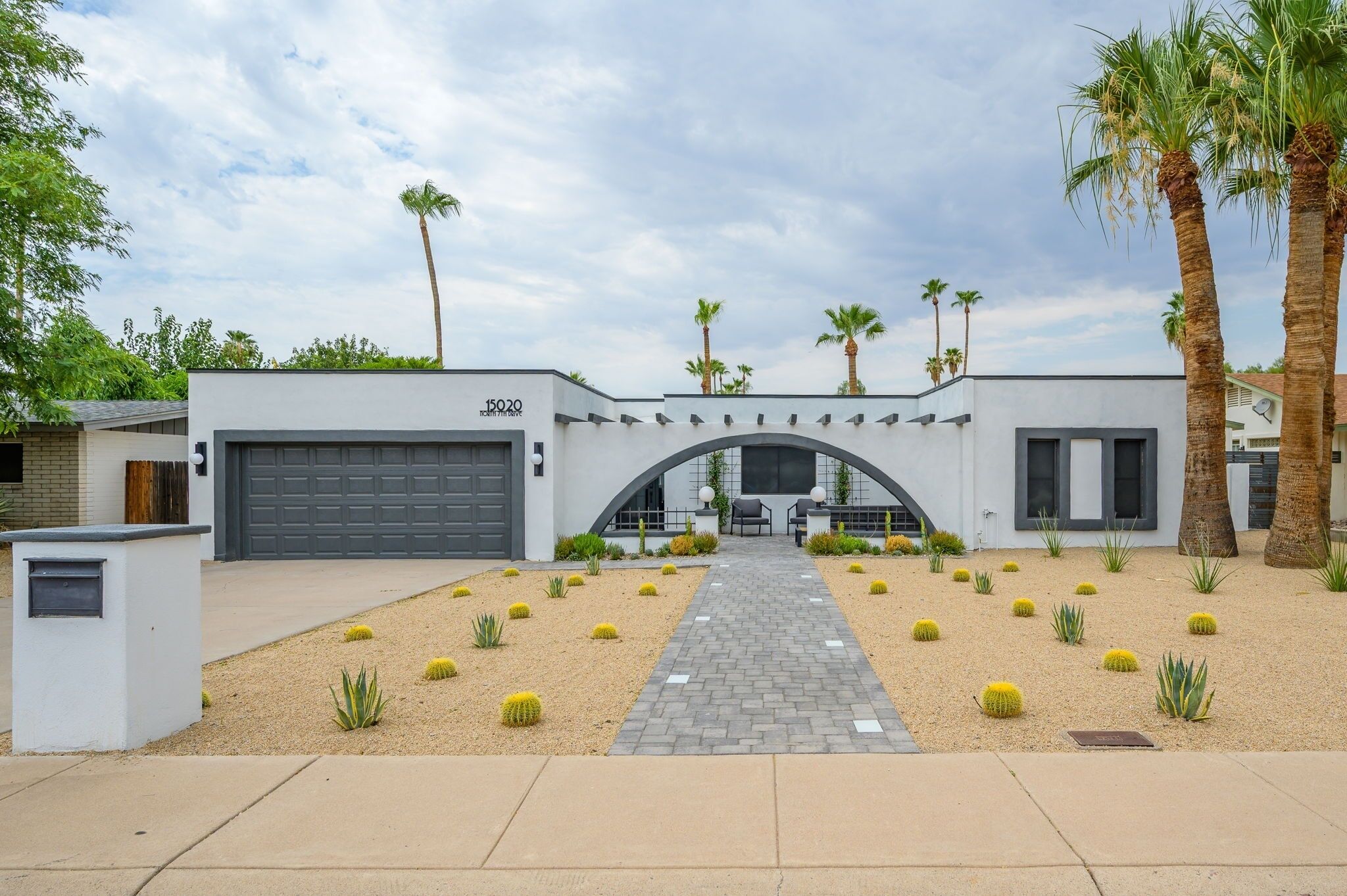 A modern house with a garage, a paved driveway, and a landscaped garden with cacti and palm trees.