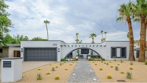 Uma casa moderna com garagem, um caminho de acesso pavimentado e um jardim ajardinado com cactos e palmeiras.