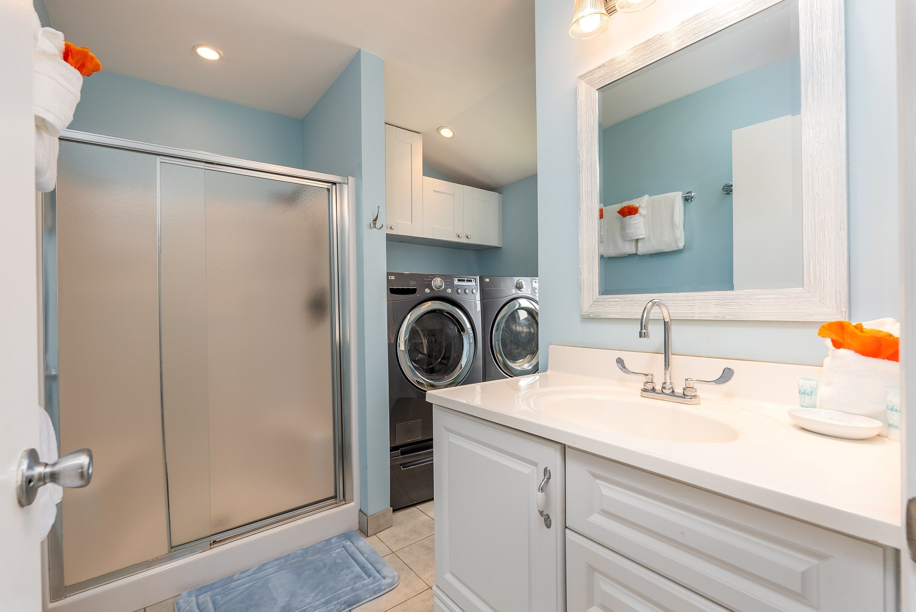 A bathroom with a shower, a sink, a mirror, and a washing machine.