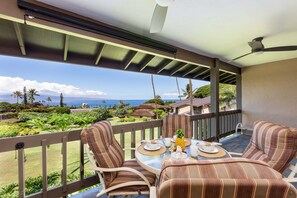 A balcony with a table set for two, overlooking a lush garden and the ocean.
