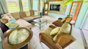 A spacious living room with a sofa, armchairs, a coffee table, and a television.