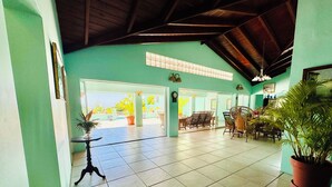 A spacious indoor area with tiled flooring, a dining area with wicker furniture, and a potted plant.