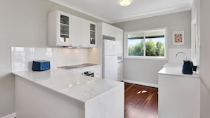 A modern kitchen with white cabinetry, a marble countertop, and a window providing a view of greenery outside.