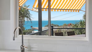 A view from a window with a yellow-striped awning, a sink, and a balcony overlooking the ocean.
