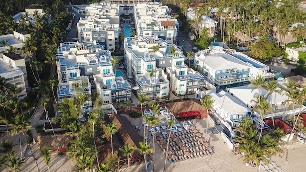 An aerial view of a coastal resort with multiple buildings, a sandy beach, and clear turquoise waters. - Presidential Suites Self Catering Punta Cana (Punta Cana)