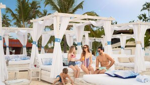 Een resort aan het strand met bungalows boven het water, palmbomen en een heldere lucht.