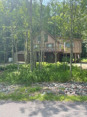 A cabin with a deck and a garage, surrounded by dense forest and ferns.
