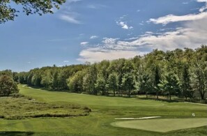 A golf course with a well-maintained fairway, sand bunkers, and a dense line of trees in the background.