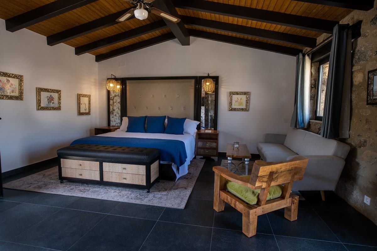 Ein Schlafzimmer mit einem großen Bett, einer hölzernen Bank, einem Stuhl und einem Nachttisch.