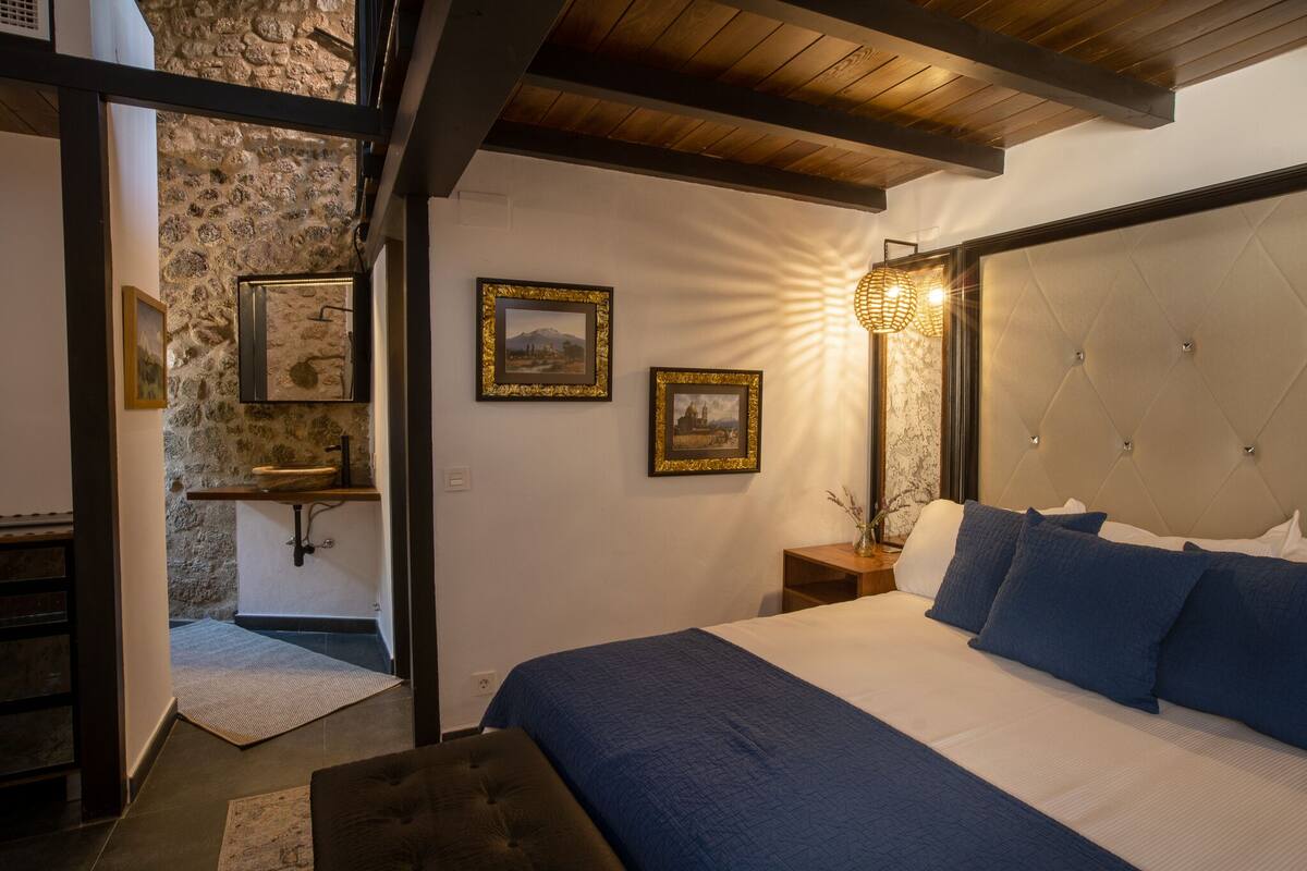 Ein Schlafzimmer mit einem großen Bett, einer Steinwand, einer Holzbalkendecke und gerahmten Bildern an der Wand.
