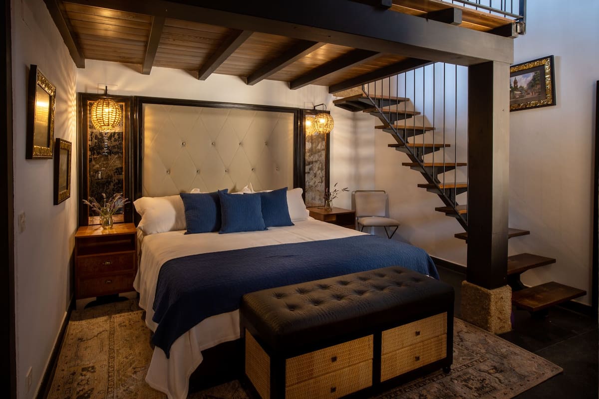 Ein Schlafzimmer mit einem großen Bett, einer Holzbank, einer Treppe und einem an der Wand hängenden Bild.