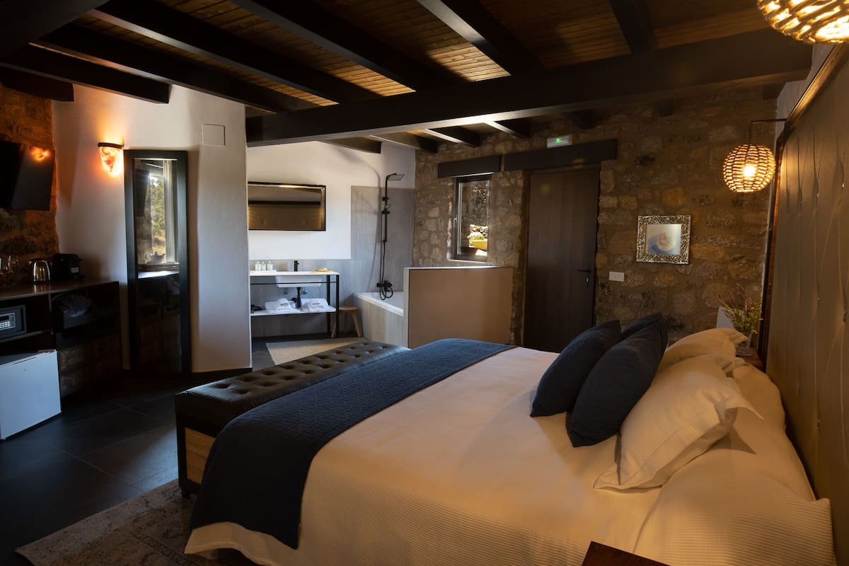 Ein modernes Schlafzimmer mit einem großen Bett, einem kleinen Schreibtisch und einem durchgehenden Türspalt sichtbaren Badezimmer.