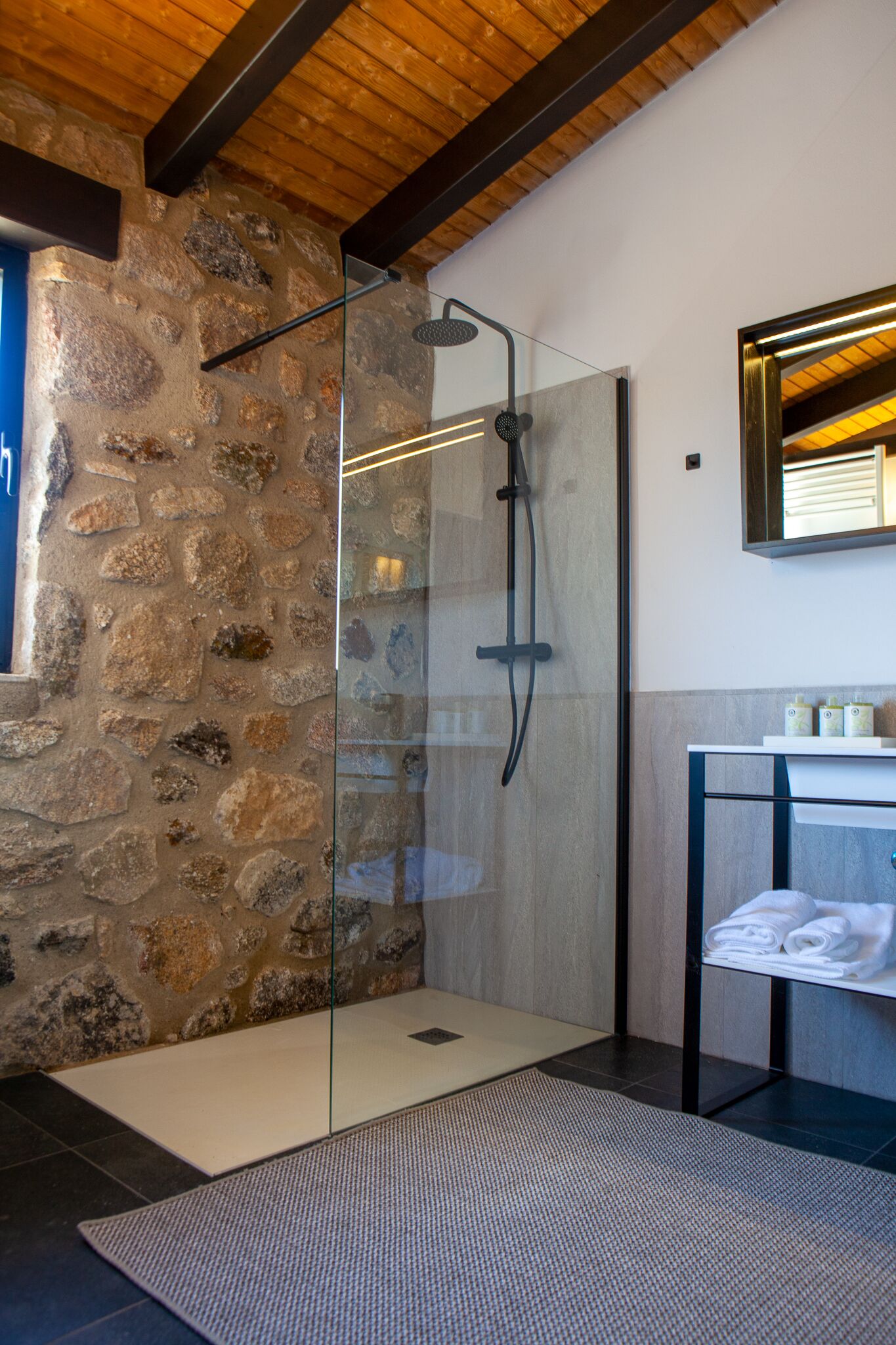 Un bagno moderno con cabina doccia in vetro, parete in pietra e soffitto in legno.