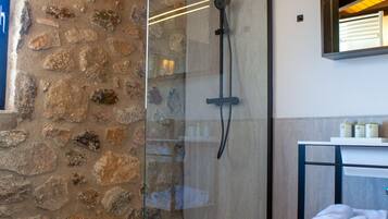 Un bagno moderno con cabina doccia in vetro, parete in pietra e soffitto in legno.