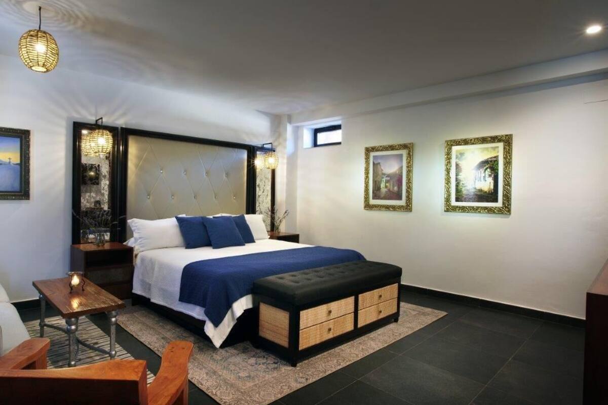 Ein modernes Schlafzimmer mit einem großen Bett, einer Couch, einem Holztisch und Kunstwerken an den Wänden.