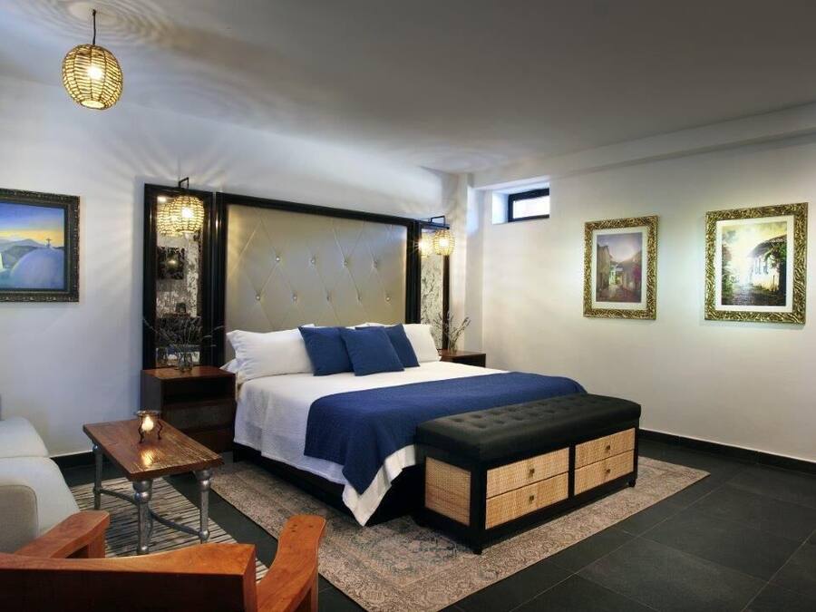 A modern bedroom with a large bed, a sofa, a wooden table, and artwork on the walls.