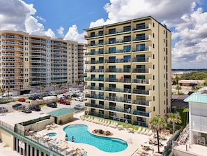 A multi-story hotel with a pool area, outdoor seating, and a view of the surrounding landscape.