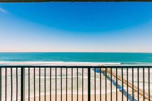 Blick auf einen Strand mit einem hölzernen Steg, der ins Meer führt, einem klaren, blauen Himmel und einem Sandstrand.