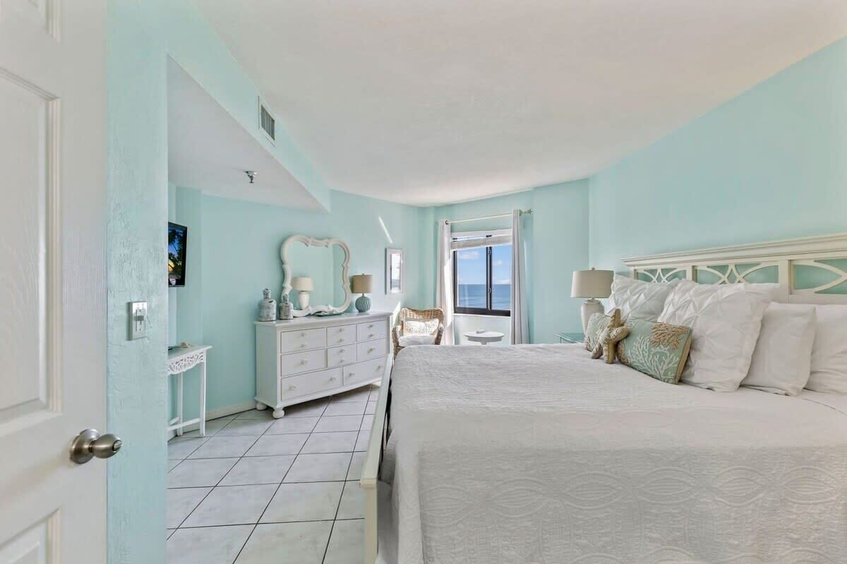 A bedroom with a bed, dresser, and a window with a view.