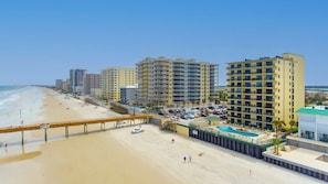 Un hotel frente a la playa con varios pisos, piscina y zona de acceso a la playa.