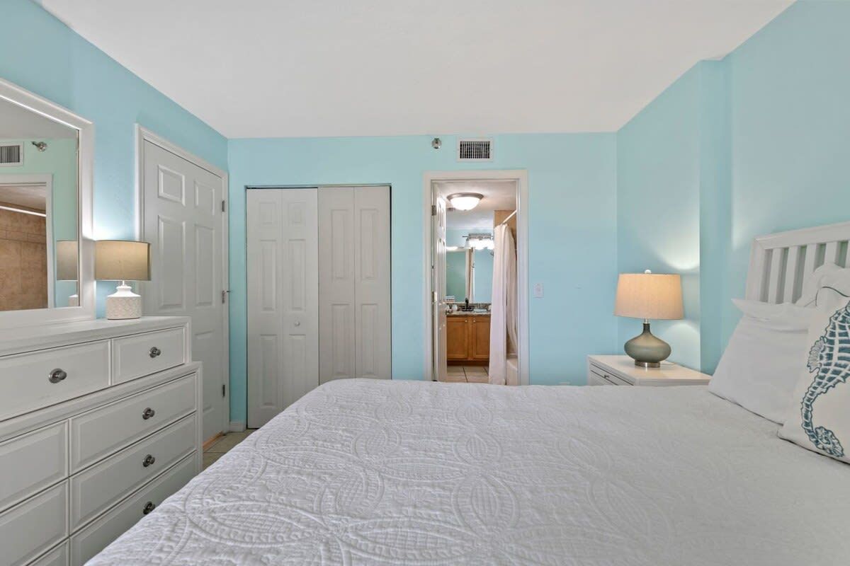 A bedroom with a bed, dresser, nightstand, and a door leading to a bathroom.