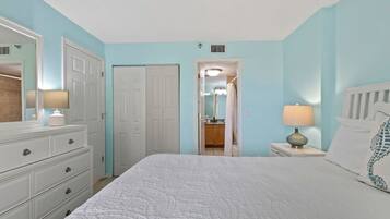 A bedroom with a bed, dresser, nightstand, and a door leading to a bathroom.