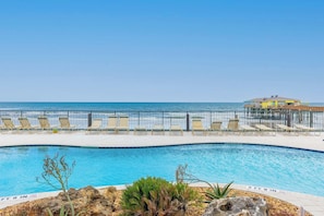 A pool area with lounge chairs and a view of the ocean.