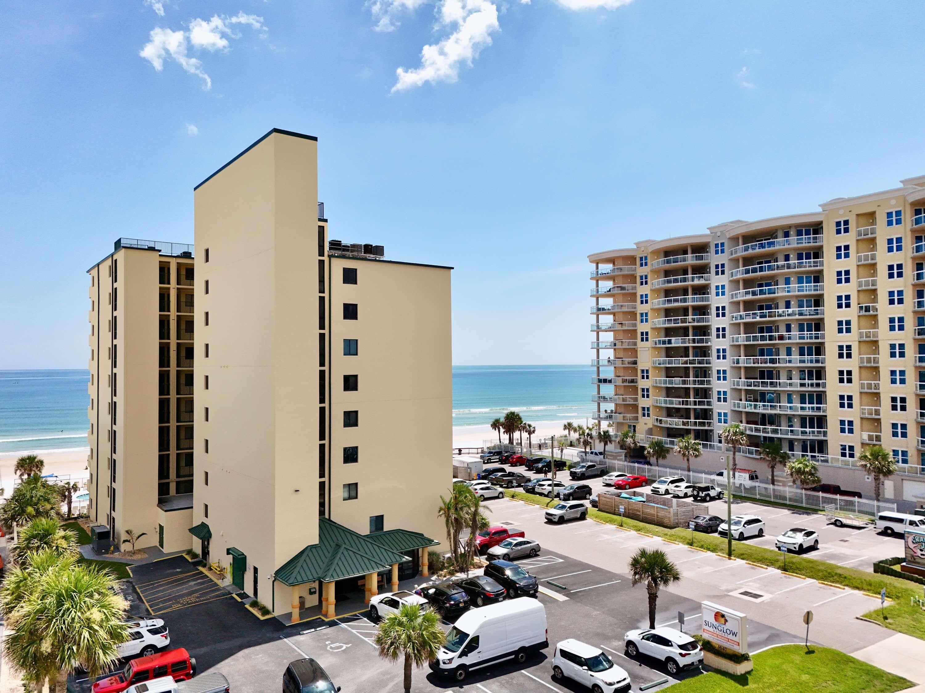 Ein mehrstöckiges Hotel mit Parkplatz, Blick auf den Strand und einem Schild für ein Restaurant.