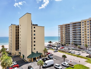 Un hôtel à plusieurs étages doté d’un parking, offrant une vue sur la plage et arborant une enseigne indiquant la présence d’un restaurant.