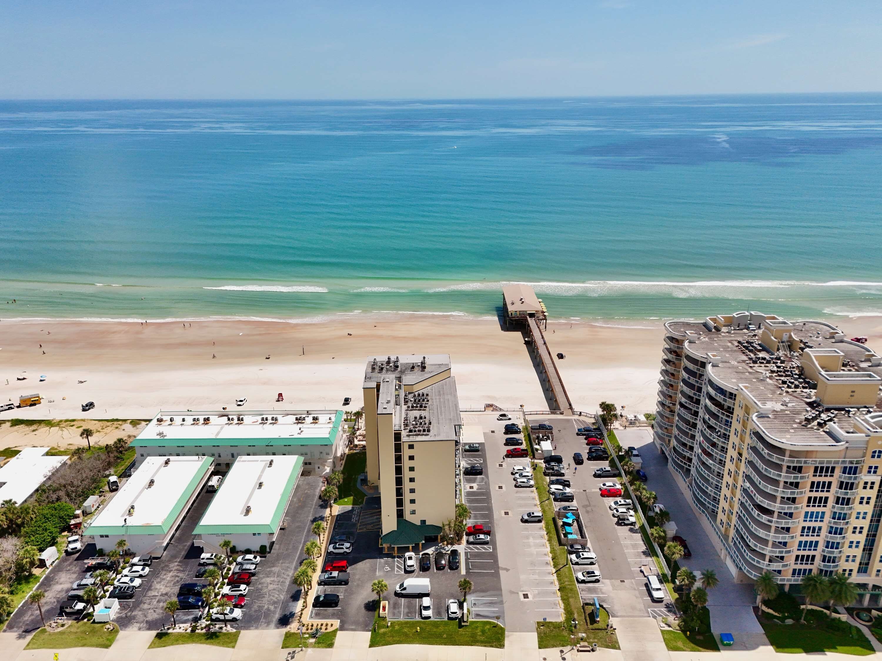 A coastal hotel with a parking lot, a beach, and a pier.