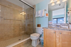 A bathroom with a glass-enclosed shower, a toilet, and a vanity with a sink and mirror.