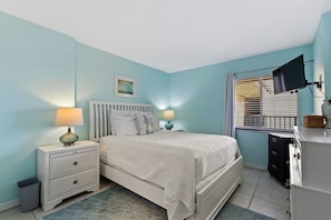 Une chambre à coucher avec un lit, des tables de chevet, une lampe, un téléviseur et une fenêtre avec des stores.