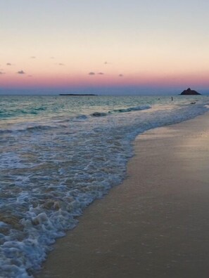 A beach with waves gently lapping at the shore and a distant island.