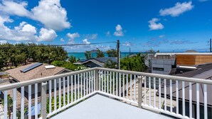 A residential area with a view of the ocean, solar panels on rooftops, and a white balcony railing. - Kailua Beach/Lanikai LUX apartment w/Ocean Views from Rooftop Sun Deck (Kailua)
