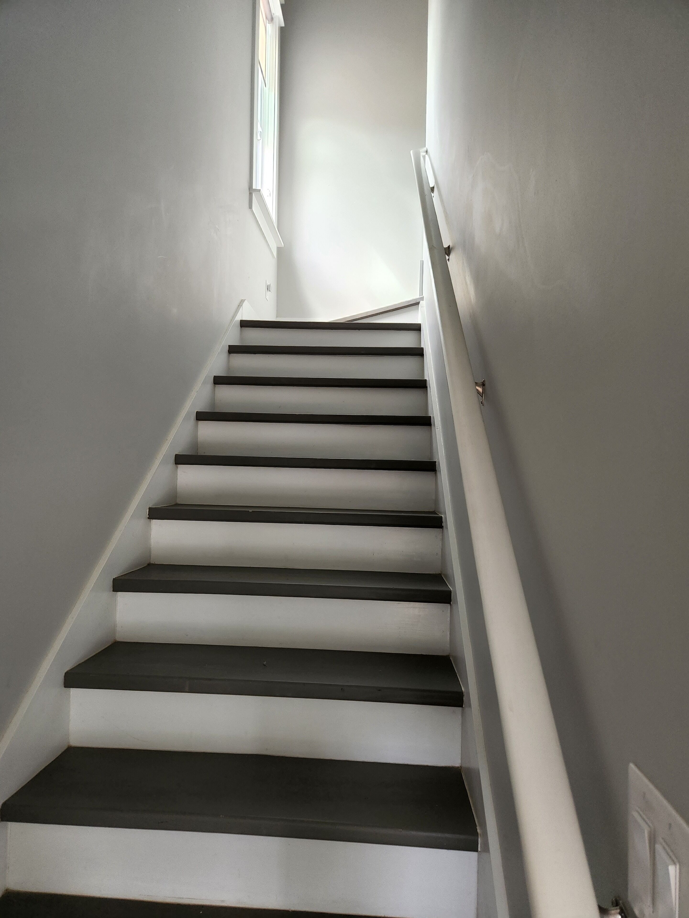 A staircase with alternating dark and light steps, white handrails, and a window at the top.