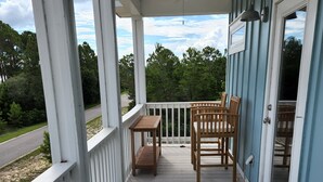 Une véranda abritée avec une table et des chaises, un ventilateur de plafond et une vue sur la verdure environnante.