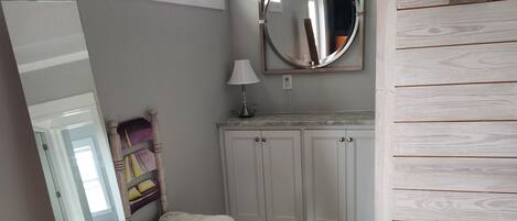 A room with a bed, a chair, a desk, a mirror, and a dresser.