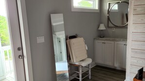 Une salle de bain avec un plancher en bois, un meuble-lavabo blanc, un miroir et une chaise.