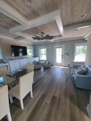 A spacious living area with a wooden ceiling, a large TV mounted on the wall, a glass dining table, and a blue sofa. - Close to beach,town and boat launch (Carrabelle)