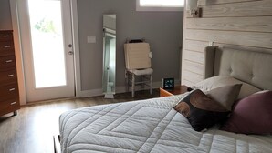 Une chambre à coucher comprenant un lit, une commode, une chaise, une table de chevet, une lampe fixée au mur et une fenêtre.